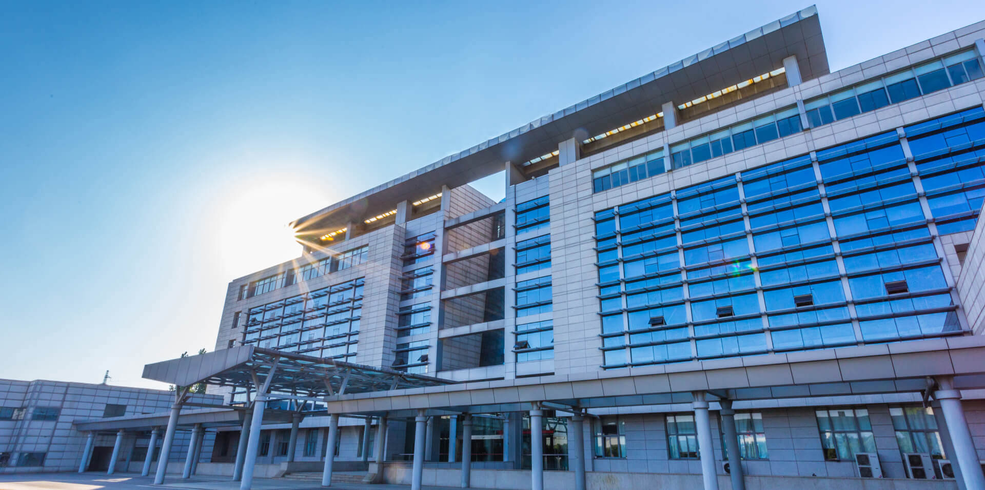 A modern multi-story building featuring extensive glass windows and a covered entrance that stands tall. The sleek architectural design mirrors the sophistication seen in JAECOO SUV HQ Office in China.